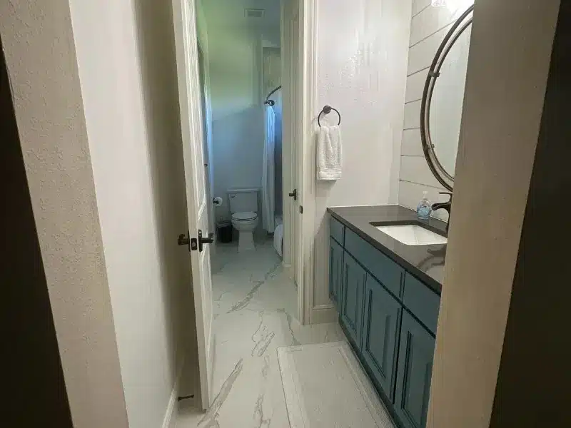 Modern bathroom with blue vanity, round mirror, and shower view, Austin, TX home interior<br />
