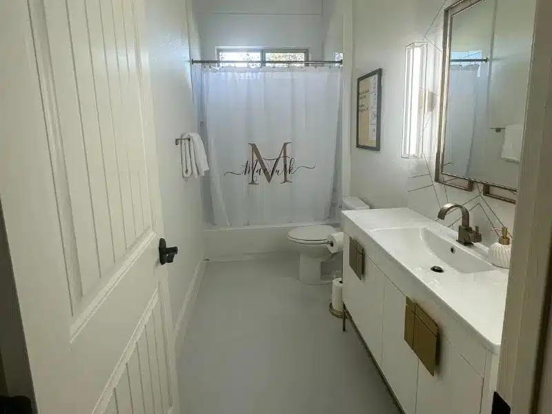 Bright white bathroom with shower curtain, vanity sink, and window light in Austin, TX home<br />
